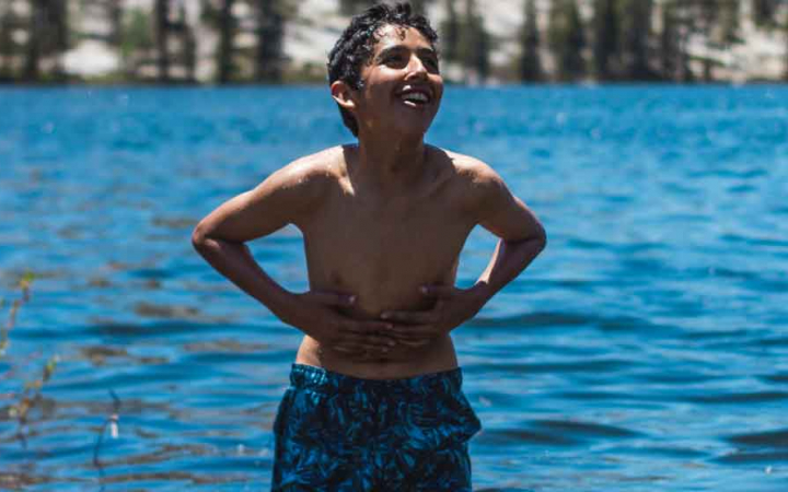 a young person stands smiling in shallow blue water